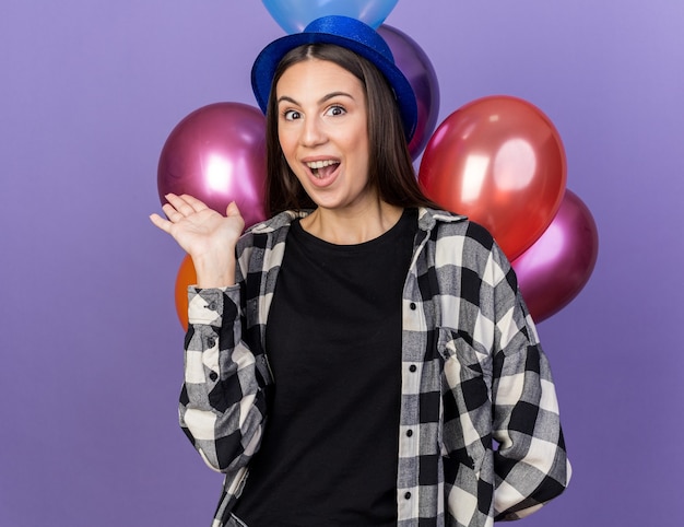 Verrast jong mooi meisje met feestmuts die voor ballonnen staat