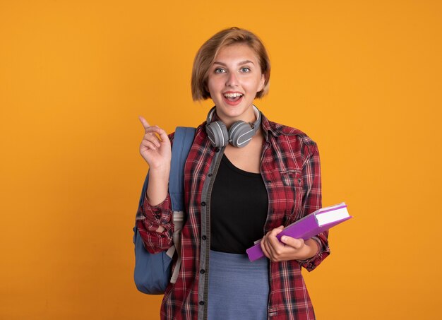 Verrast jong slavisch studentenmeisje met een koptelefoon die een rugzak draagt, houdt boek- en notitieboekjes aan de zijkant vast