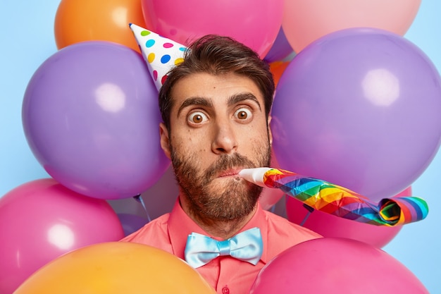 Gratis foto verrast jonge kerel poseren omringd door kleurrijke verjaardagsballons