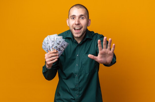 Verrast jonge knappe kerel met een groen shirt met contant geld dat een stopgebaar toont