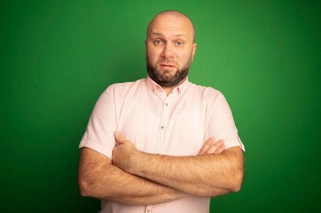 Verrast kale man van middelbare leeftijd met roze t-shirt handen kruisen