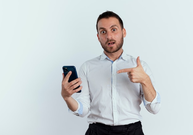 Verrast knappe man houdt en wijst naar telefoon geïsoleerd op een witte muur