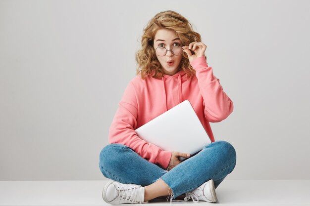 Verrast krullend meisje met laptop, op zoek opgewonden