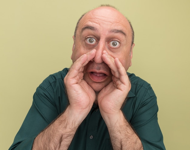 Verrast man van middelbare leeftijd met een groen t-shirt die iemand belt die op een olijfgroene muur is geïsoleerd