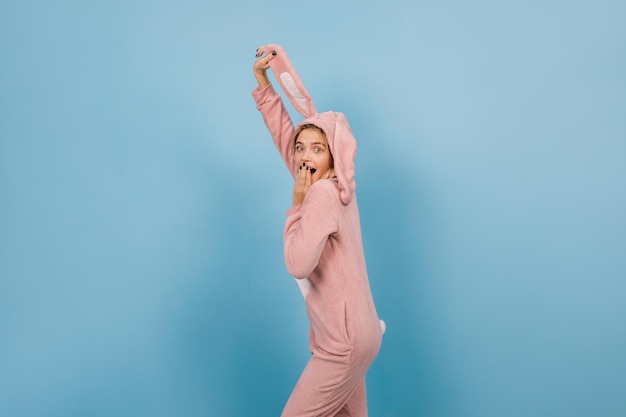 Verrast meisje in konijnenkostuum met oren op blauwe achtergrond Studio shot van mooie jonge vrouw draagt bunny kigurumi