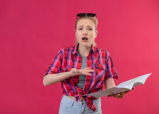 Verrast reizigers jong meisje met rood shirt en bril op haar hoofd met kaart op geïsoleerde roze achtergrond