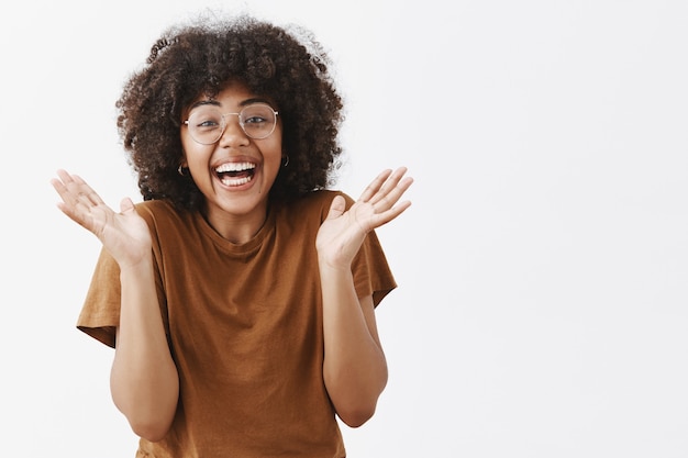 verrast speels en ontroerd knappe Afro-Amerikaanse vrouw in glazen en stijlvol bruin t-shirt handen in elkaar grijpend en lachend van vreugde en opwinding houdt van geweldige show