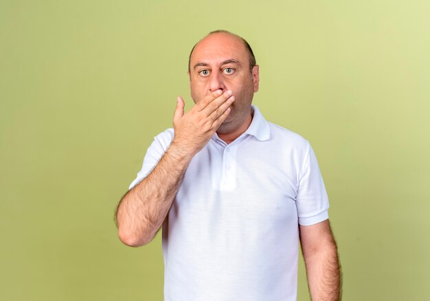 Verrast volwassen man bedekt mond met hand geïsoleerd op olijfgroene muur