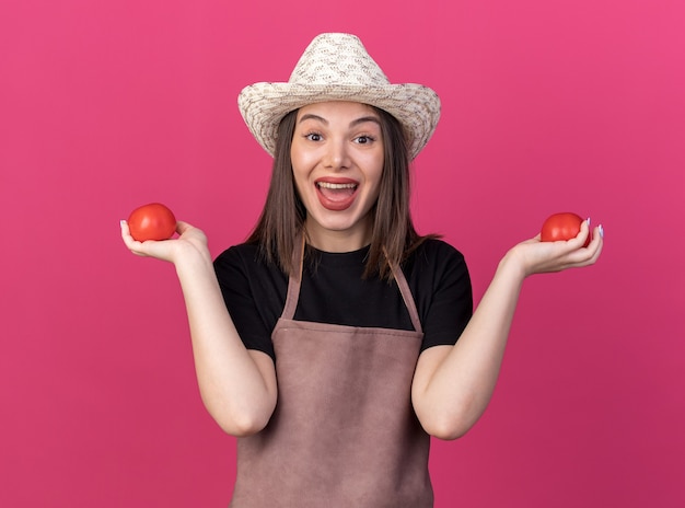 Verrast vrij Kaukasische vrouwelijke tuinman tuinieren hoed met tomaten op roze te dragen