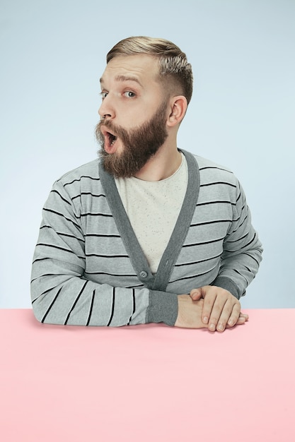 Verrast zakenman zittend aan tafel op blauwe studio.