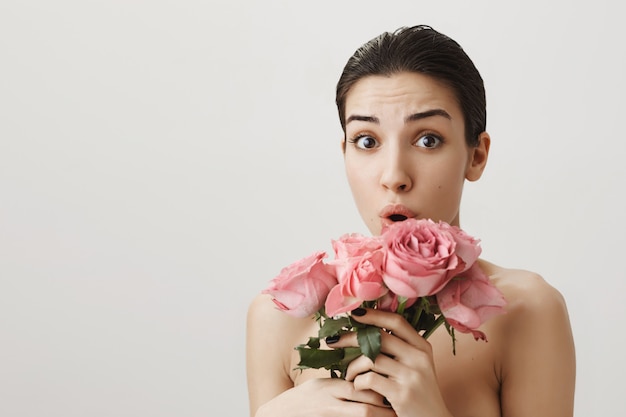 Verraste en bezorgde vrouw die naakt met een boeket rozen staat en bezorgd kijkt