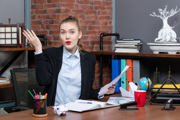 Verraste jonge dame die aan een tafel zit en het document vasthoudt om iemand op kantoor te vragen