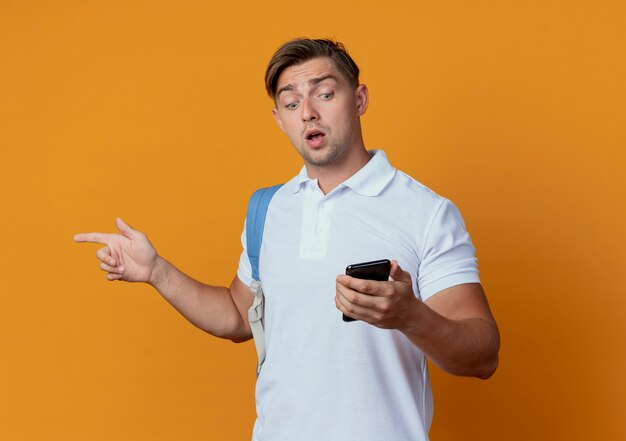 Verraste jonge knappe mannelijke student die achterzak draagt en telefoon bekijkt