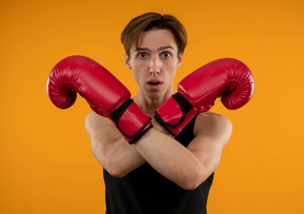 Verraste jonge sportieve kerel die bokshandschoenen draagt die gebaar van geen toont dat op oranje muur wordt geïsoleerd