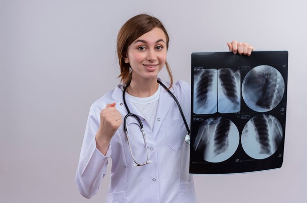 Verraste jonge vrouwelijke arts die medische mantel en stethoscoop draagt en röntgenfoto op geïsoleerde witte muur met exemplaarruimte houdt