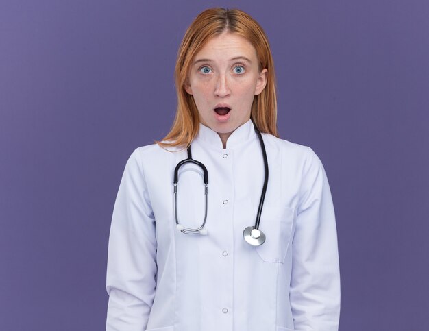 Verraste jonge vrouwelijke gemberdokter die medische mantel en stethoscoop draagt