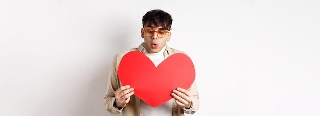 Verraste knappe man ontvangt op valentijnsdag een grote rode hartkaart en kijkt naar een geschenk met amazeme