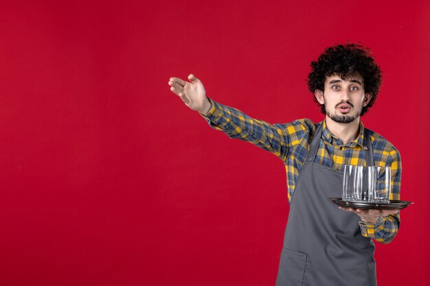 verraste ober met krullend haar die een dienblad vasthoudt met een bril die iets wijst op een geïsoleerde rode achtergrond