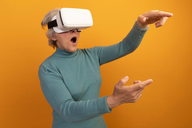 Verraste oude vrouw met een blauwe coltrui en een vr-headset die naar de zijkant kijkt en wijst op een oranje muur