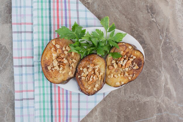 Verrukkelijk gearomatiseerde schotel van gebakken Indiase aubergineplakken gegarneerd met gehakte knoflook en peterselie, op marmer.