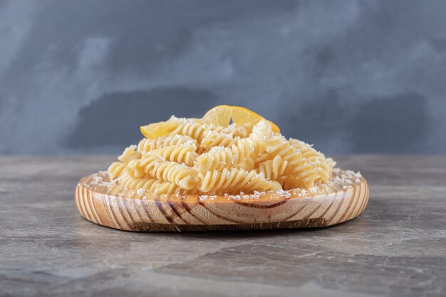 Verrukkelijke fusilli pasta met schijfjes citroen op de houten plaat, op het marmeren oppervlak.