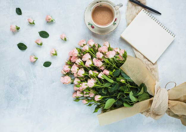 Vers boeket van roze rozen met een kopje koffie; spiraal Kladblok en pen op gestructureerde achtergrond