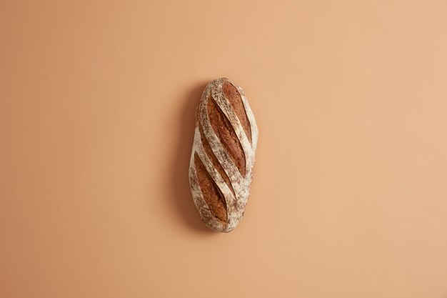 Vers zelfgemaakt knapperig Frans volkorenbrood bereid van biologische bloem, gemaakt op zuurdesem, geïsoleerd op bruine studioachtergrond. Bakkerij en voedselconcept. Thuis koken en eten bereiden.