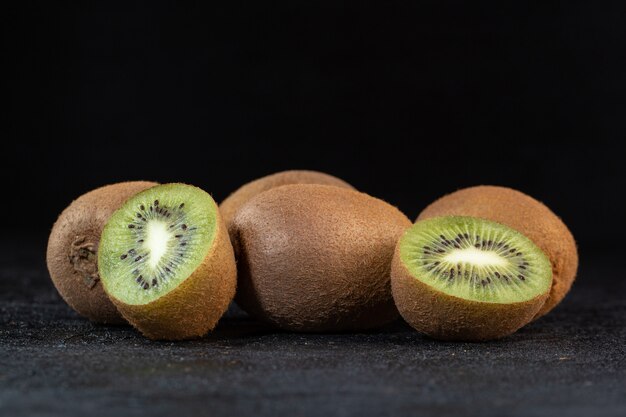Verscheidene bruine kiwi verse rijpe sappige zachte halve besnoeiing die op donker bureau wordt geïsoleerd