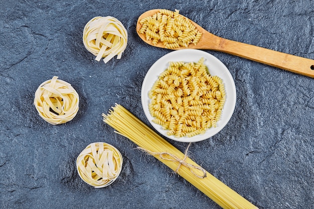 Verscheidenheid aan rauwe pasta met houten lepel op blauwe achtergrond