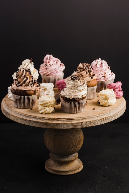 Gratis foto verscheidenheid van cupcakes op houten tribune tegen zwarte achtergrond