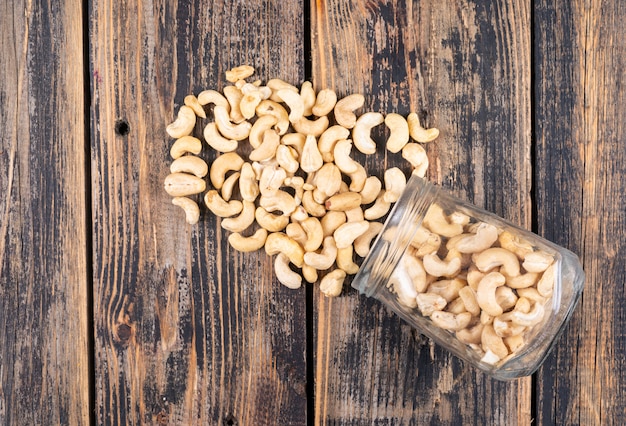 Verschillende cashewnoten met pot op houten tafel, bovenaanzicht.