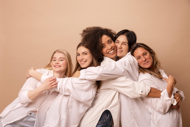 Verschillende interage vrouwen in witte overhemden met unieke natuurlijke schoonheid omhelzen elkaar op beige achtergrond