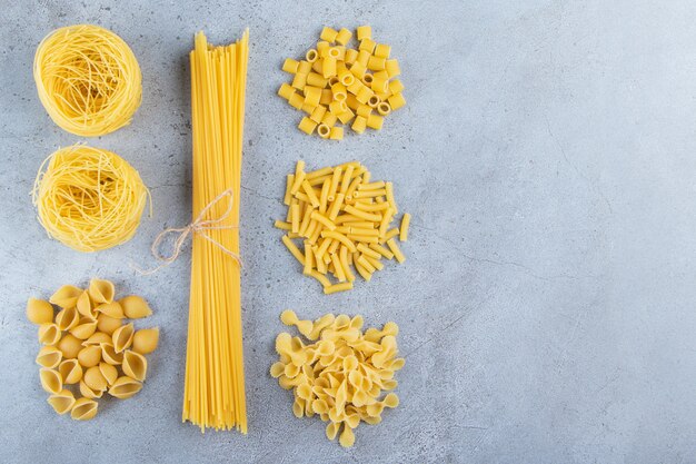 Verschillende soorten rauwe droge pasta op een stenen achtergrond.