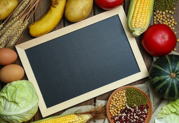 Gratis foto verse biologische groenten, fruit, eieren, bonen en corns met bord op vintage houten tafel