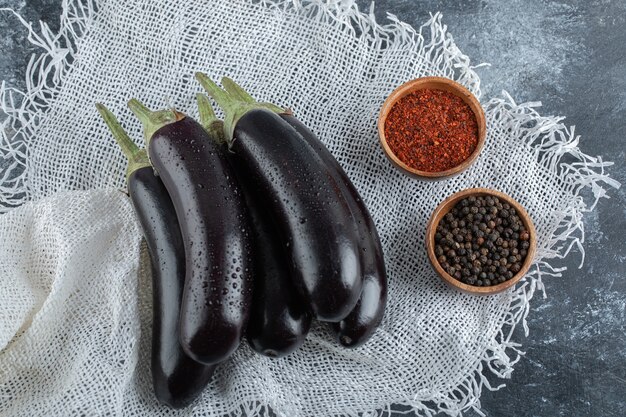 Verse biologische paarse aubergines met kruiden, rode en zwarte peper op zak.