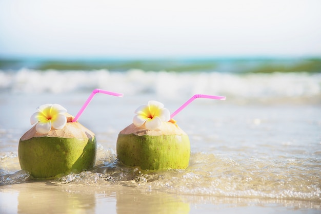 Verse die kokosnoot met plumeriabloem op schoon zandstrand met overzeese golf wordt verfraaid - vers fruit met van de overzeese het concept zonvakantie