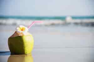 Gratis foto verse die kokosnoot met plumeriabloem op schoon zandstrand met overzeese golf wordt verfraaid - vers fruit met van de overzeese het concept zonvakantie