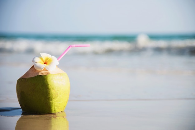 Verse die kokosnoot met plumeriabloem op schoon zandstrand met overzeese golf wordt verfraaid - vers fruit met van de overzeese het concept zonvakantie