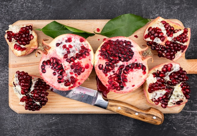 verse granaatappels met mes bovenaanzicht op houten snijplank op donker