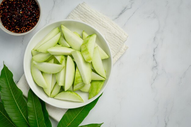 Verse groene mango met zoete vissaus die op witte oppervlakte dompelt