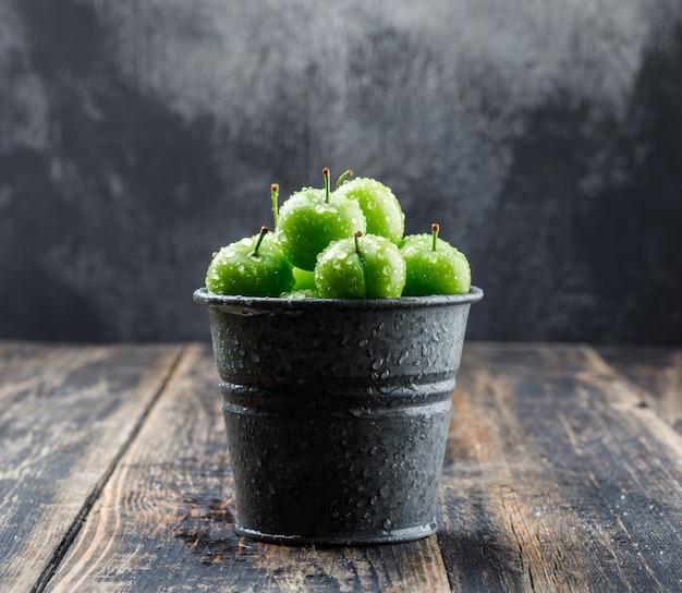 Verse groene pruimen in een mini-emmer zijaanzicht op houten en mistige muur