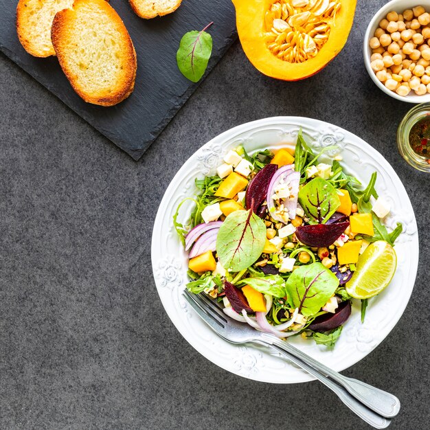 Verse groentesalade met bieten, rucola, rode ui en zuring in een wit bord met pompoen, toast en kikkererwten