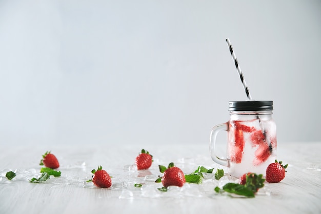 Verse koude zelfgemaakte limonade van aardbei en bruisend water in rustieke pot met streepstro op wit wordt geïsoleerd.