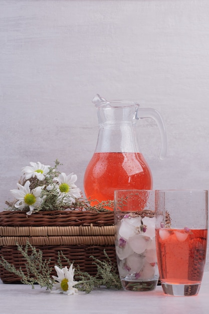 Verse limonade in glas en pot met madeliefjes op witte tafel.