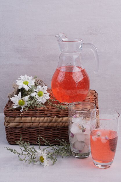 Verse limonade in glas en pot met madeliefjes op witte tafel.