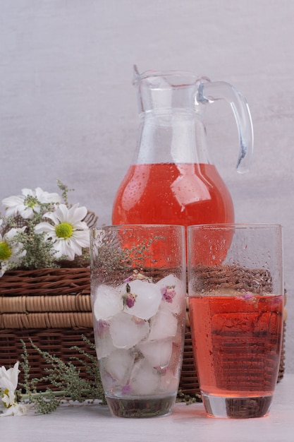 Verse limonade in glas en pot met madeliefjes op witte tafel.