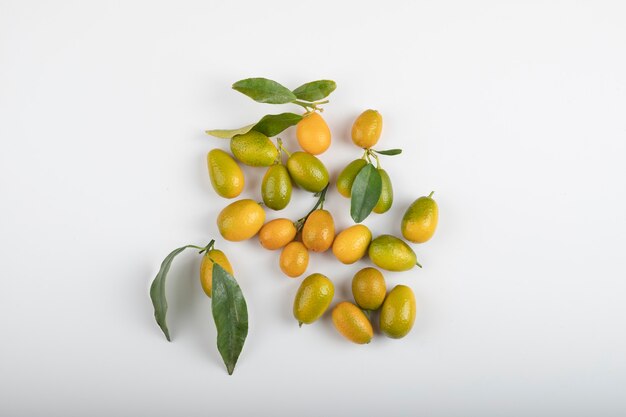 Verse rijpe kumquats met bladeren op witte tafel.
