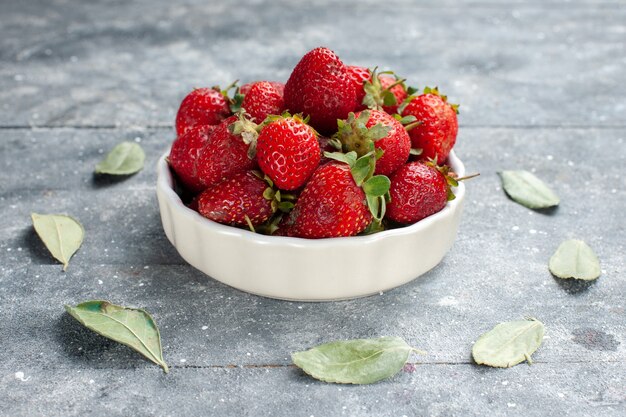 verse rode aardbeien in witte plaat samen met groene gedroogde bladeren op grijs bureau, fruit verse bessen kleur foto vitamine gezondheid