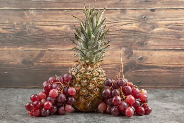 Verse rode druiven met rijpe ananas op marmeren oppervlak.