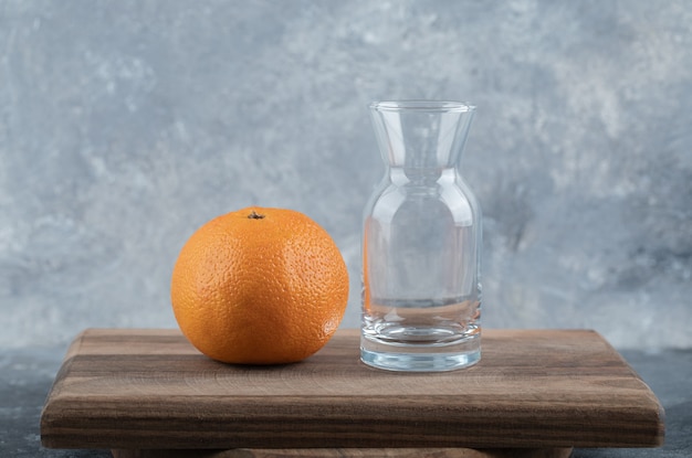 Verse sinaasappel en glas op een houten bord.